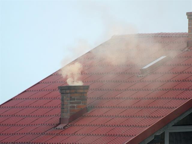 Hausdach mit roten Dachziegeln, aus dem Kamin kommt Rauch